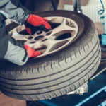 Technician in red gloves placing a tire on a balancing machine, showcasing precision service included in the Rubens Tires Tire Rotation Balance Offer for improved safety and performance.