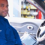 Ruben’s Tires technician smiling from the driver’s seat with a diagnostic tablet, showcasing professional service and convenience with Rubens Tires Booking Altamonte.